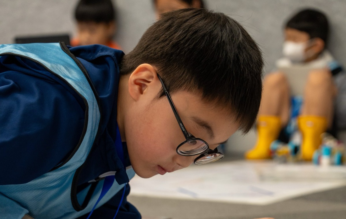 Rookie student leaning in to adjust his robot mid-run