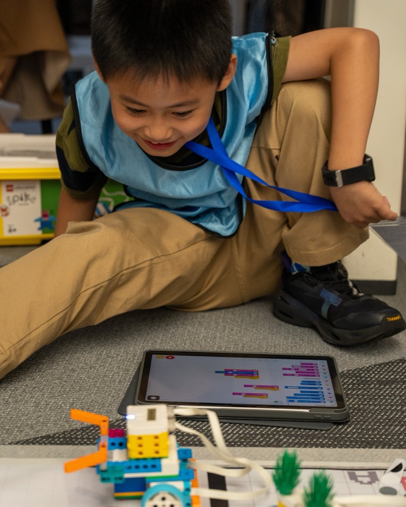 A young competitor deep in a task-based challenge — coding on a tablet beside his robot
