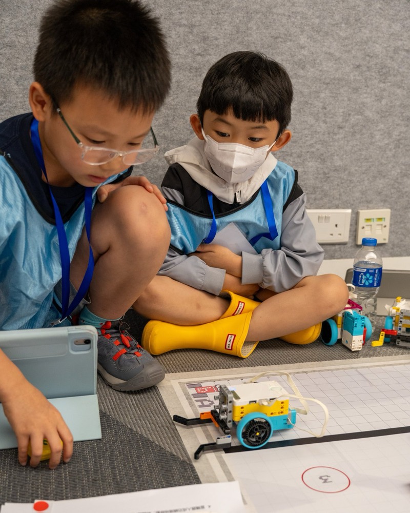 Two teammates huddled together over their robot and the game mat