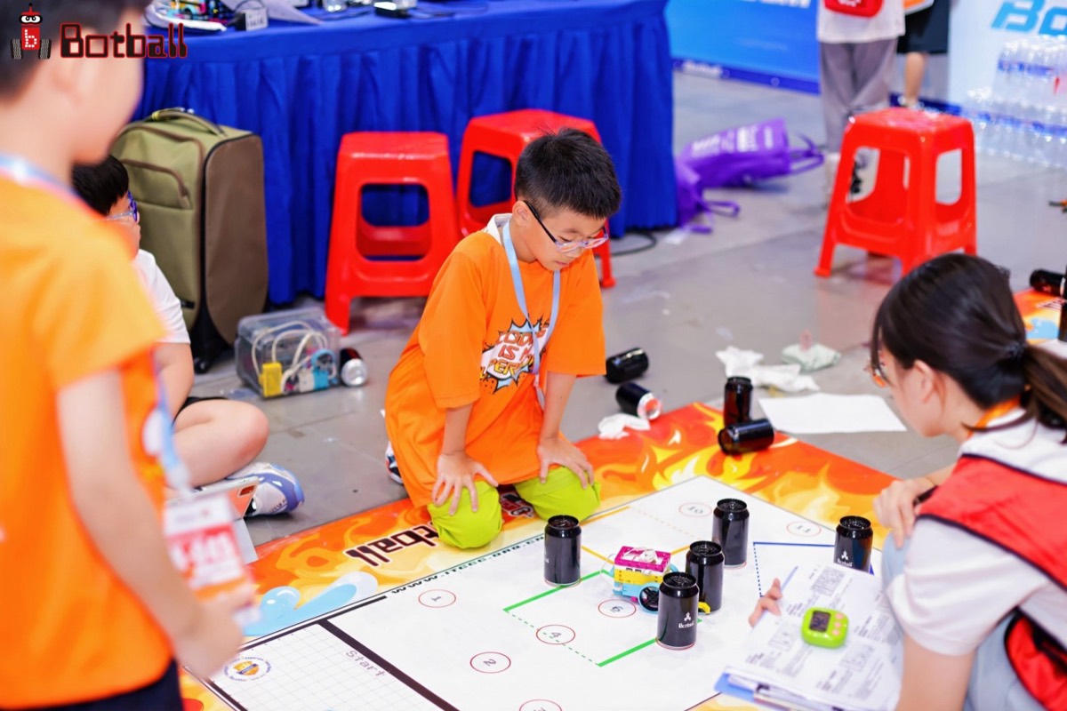 Students gathered around the official Botball game table, robots mid-match